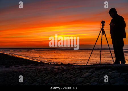 Tourist mit Kamera bei Sonnenuntergang auf Trischedamm, Nordsee bei Ebbe Stockfoto