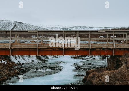 Eine schöne rote Brücke über einen Gletscherfluss in Island. Eine nordische, kalte, winterliche Landschaft. Stockfoto