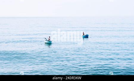 Einfacher Hintergrund ruhig dunkelblau Meer Fischerboote allein weiß blass Spindrift Wolken Open Way keine Einschränkungen Stockfoto