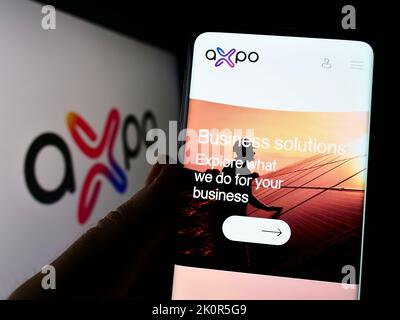 Person, die Mobiltelefon mit der Webseite des Schweizer Energieunternehmens Axpo Holding AG auf dem Bildschirm vor dem Logo hält. Konzentrieren Sie sich auf die Mitte des Telefondisplays. Stockfoto