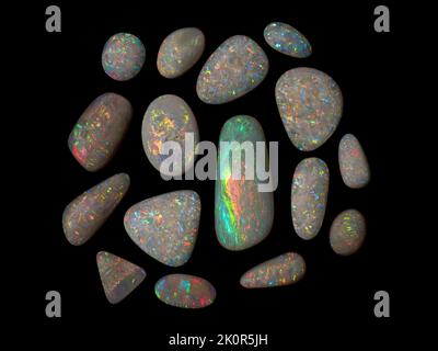 Australische Opal-Edelsteine, aufgenommen auf einem schwarzen Hintergrund, um die wunderschöne Farbe und das Muster dieses Natursteins hervorzuheben. Projekt mit Damien Hirst. Stockfoto