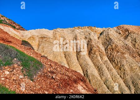 Details der wunderschön farbigen Klippen an sonnigen Tagen, klarer blauer Himmel. Verwitterte Hänge des Strandes von Agios Ioannis, Milos, Griechenland, aus gelbem und rotem Stein Stockfoto