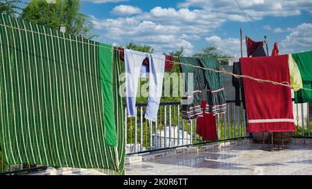 Bunte Klamotten zum Trocknen auf einer Wäscheleine und Sonne am blauen Himmel. Stockfoto