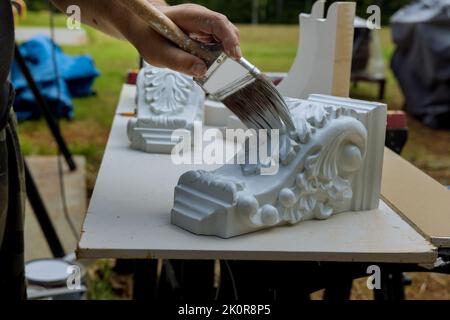 Mit einem Pinsel malt ein Arbeiter hölzerne Korbschalen für eine Kücheninsel auf eine Tischfläche Stockfoto