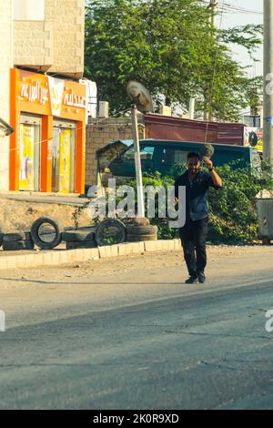 06.18.2022. Ein Einheimischer, der in Jordanien die Straße entlang läuft. Kleiner Markt und eine Siedlung im Hintergrund. Hochwertige Fotos Stockfoto