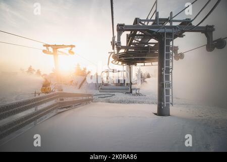 Sonnenaufgang bricht durch den dicken weißen Nebel auf dem Gipfel des Vuokatti Hill, einem Skigebiet in Vuokatti, Finnland. Blick auf den gefrorenen Sessellift. Die Scand Stockfoto