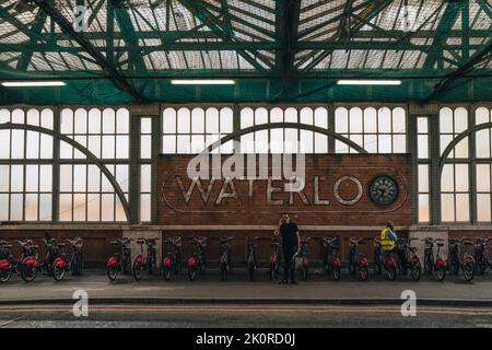 London, Großbritannien - 8. September 2022: Wandschild und Uhr vor Waterloo, Großbritanniens größter und verkehrsreichster Station, ist die Santander-Fahrraddockstation darunter. Stockfoto