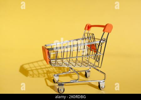 Kleiner Supermarkt Lebensmittelgeschäft Push Cart zum Einkaufen. Shopaholic. Käufer. Einkaufskonzept. Nahaufnahme. Isolierter Einkaufswagen auf gelbem Hintergrund. Cop Stockfoto