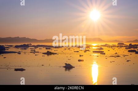 Goldener Sonnenuntergang über der Masse der Eisberge, die im arktischen Meer vor der Küste Grönlands schweben Stockfoto
