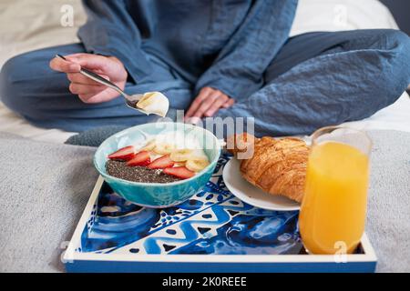 Nahaufnahme einer jungen Frau, die im Schlafanzug eine Frühstückschüssel im Bett isst Stockfoto