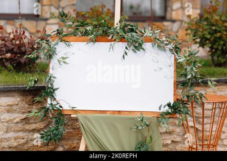 Hochzeit Holzbrett, mockup, Einladung Staffelei, mit weißem Raum für eine Inschrift, mit frischem Grün und grünen Tuch dekoriert. Hochzeitsrahmen outd Stockfoto