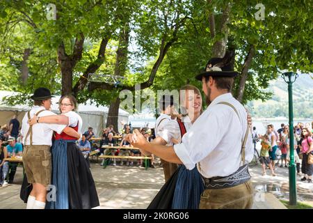 Junge Männer und Frauen tanzen in Tirol Kostüme bei einem Festmahl im Park von Zell am See in Österreich Stockfoto