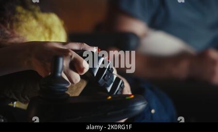Nicht erkennbarer Mann hilft Frau mit Behinderung im motorisierten Rollstuhl mit Gamepad und nachdem sie begann, in Videospiel zu spielen, Nahaufnahme. Stockfoto
