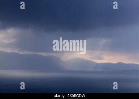 September und Sonnenstrahlen passieren regnerische Wolken. See auf dieser Seite und Berg im Hintergrund. Stockfoto