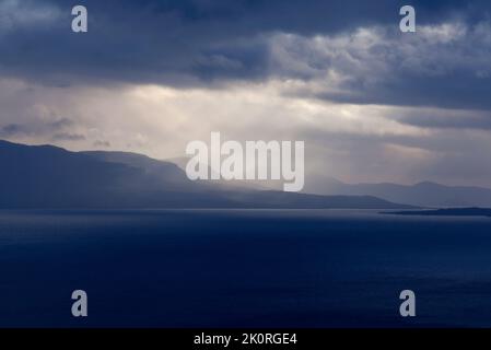 September und Sonnenstrahlen passieren regnerische Wolken. See auf dieser Seite und Berg im Hintergrund. Stockfoto