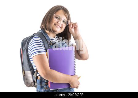 Das Schulmädchen fixiert ihre Brille, während sie ihre Studienbücher hält und einen Rucksack trägt. Stockfoto