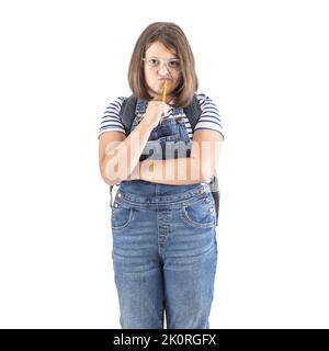 Schulmädchen in Brille hält gekreuzte Arme und Bleistift dicht an ihren Mund und denkt hart. Stockfoto