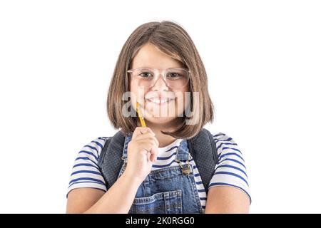 Lächelnd niedliches junges Schulmädchen in Brille hält Bleistift nahe an ihrem Mund. Stockfoto