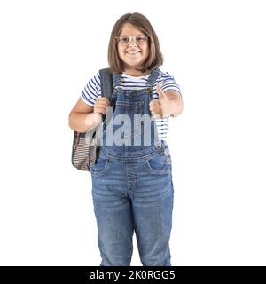 Das Mädchen, das an der Schule teilnimmt, trägt einen Rucksack und zeigt einen Daumen nach oben auf einem isolierten weißen Hintergrund. Stockfoto