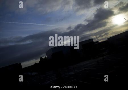 Dramatischer blauer Himmel bei Sonnenaufgang mit Wolken über der silhouettierten Industrielandschaft. Stockfoto