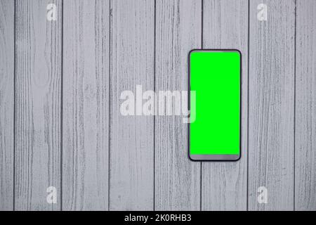 Smartphone mit grünem Bildschirm, Mockup-Bild auf Holztisch mit Platz zum Kopieren, um Inhalte hinzuzufügen. Smartphone- und Lifestyle-Konzept. Stockfoto