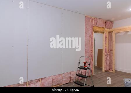 Die Trockenwand wird an den Balken der Wand verschraubt, nachdem die Schall- und Wärmedämmung im neuen Haus installiert wurde. Stockfoto