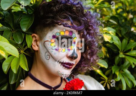 Nahaufnahme einer jungen lateinischen kaukasischen Frau mit La calavera catrina Make-up mit einer Blume, Stockfoto