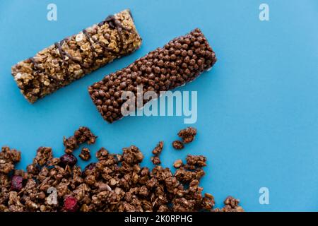 Draufsicht auf Müsliriegel in der Nähe von knusprigem Müsli, isoliert auf blau, Stockbild Stockfoto