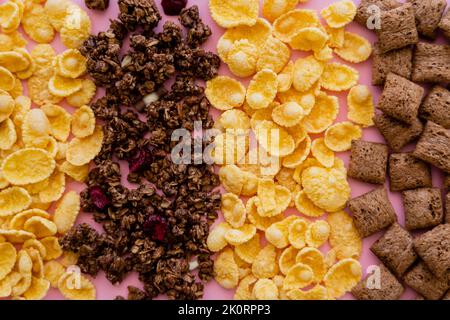 Draufsicht auf verschiedene Frühstücksflocken mit Cornflakes und Müsli auf rosa, Stockbild Stockfoto