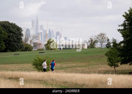 Mit Wolkenkratzern in der City of London, dem Finanzviertel der Hauptstadt, in der Ferne joggen zwei Läufer am 8.. September 2022 in London, England, über den Brockwell Park im Süden Londons. Stockfoto