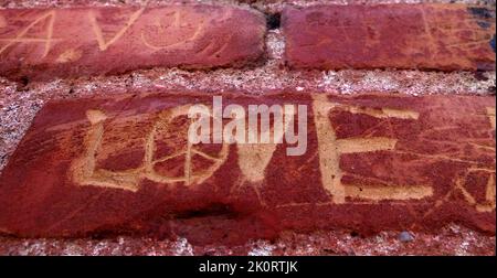 Detail der alten roten Ziegelwand mit den Worten Namen und Liebe zerkratzt oder geschnitzt Stockfoto