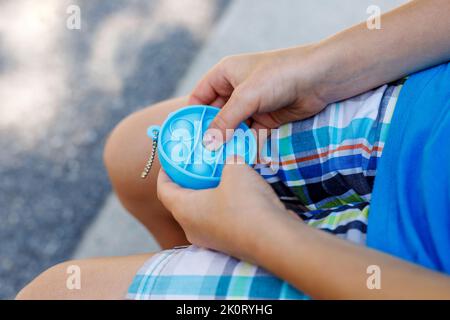 Kind spielt mit Pop it sensorische Antistress-Spielzeug. Stressabbau zappelte in den Händen eines Kindes. Konzept der psychischen Gesundheit und Angst Stockfoto