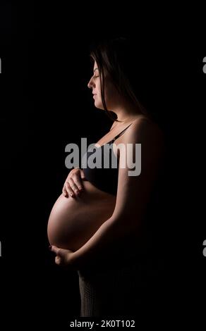 Junge Brünette Frau, die ihre Augen schließt und ihren Baby-Beule hält. Stockfoto