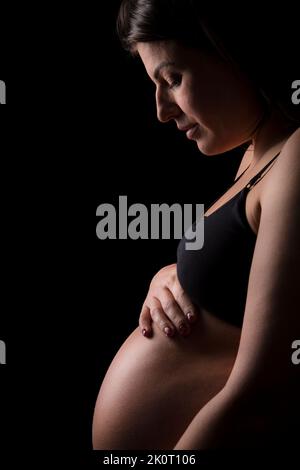 Junge Brünette Frau schaut hinunter auf ihr Baby Beule. Stockfoto