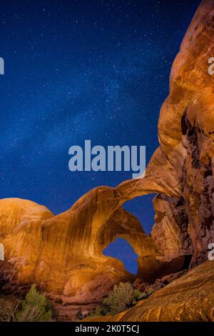 Doppelbogen bei Nacht mit der Milchstraße, beleuchtet vom Mond und Lichtbild. Arches National Park, Moab, Utah. Stockfoto