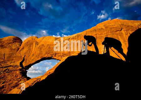 Silhouette von Fotografen, die beim Sonnenaufgang im Arches National Park, Moab, Utah, ein Foto des Nordfensters machen. Stockfoto