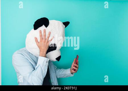 Besorgter Mann in Panda-Maske, der schlechte Nachrichten auf dem Handy liest Stockfoto