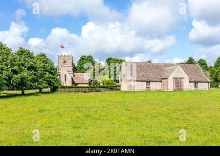 Die normannische Kirche St. Michael and All Angels und eine Scheune aus dem 18.. Jahrhundert im Cotswold-Dorf Guiting Power, Gloucestershire, Großbritannien Stockfoto