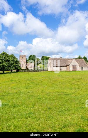 Die normannische Kirche St. Michael and All Angels und eine Scheune aus dem 18.. Jahrhundert im Cotswold-Dorf Guiting Power, Gloucestershire, Großbritannien Stockfoto