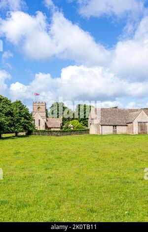 Die normannische Kirche St. Michael and All Angels und eine Scheune aus dem 18.. Jahrhundert im Cotswold-Dorf Guiting Power, Gloucestershire, Großbritannien Stockfoto