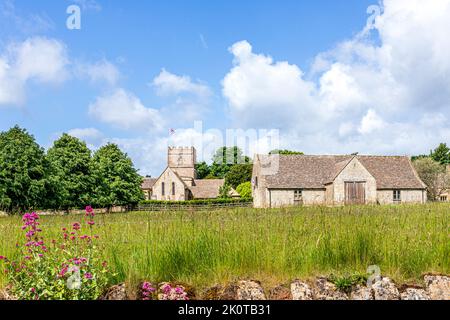 Die normannische Kirche St. Michael and All Angels und eine Scheune aus dem 18.. Jahrhundert im Cotswold-Dorf Guiting Power, Gloucestershire, Großbritannien Stockfoto