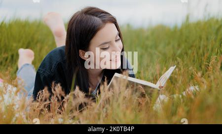 Junge attraktive Brünette kaukasische Frau Mädchen auf Gras liegen hübsche Teenager Freundin Student lesen interessante Buch pädagogische Literatur Roman Stockfoto