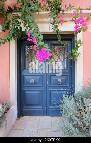 Traditionelles griechisches Haus mit Blumen auf der Insel Korfu, Griechenland. Blaue Tür, umgeben von magentafarbenen Blumen Stockfoto