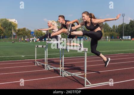 Zwei AthletInnen, Frau und Mann, die im Freien im Stadion Hürden laufen Stockfoto