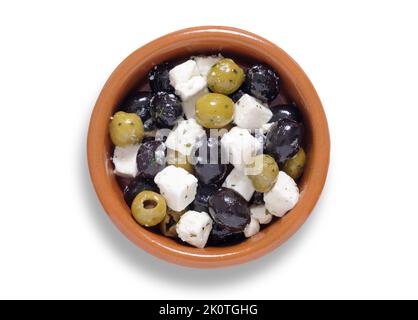 Grüne und schwarze Oliven mit Feta-Käsewürfeln in einer kleinen braunen Schüssel, von oben isoliert auf Weiß mit ausgeschnittenem Pfad geschossen Stockfoto