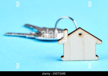 Schmuckkette in Form eines Holzhauses mit den Schlüsseln zur Wohnung auf dem blauen Hintergrund Stockfoto