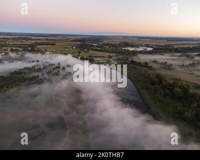 Bilder vom Drohnenflug über den Nebel. Fluss, Wald, Felder und Wiesen in nebliger Sommerdämmerung. Stockfoto