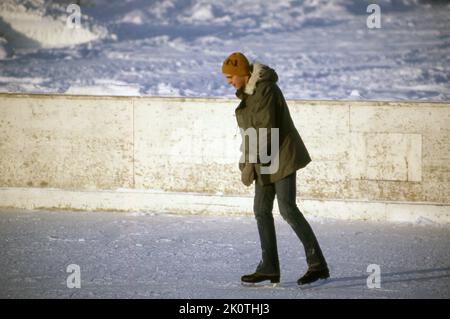 1970, historisch, ein männlicher Skater... Draußen steht ein junger Mann im Mantel und mit einem Hut auf dem Eis in einem geschlossenen Eisring. Stockfoto