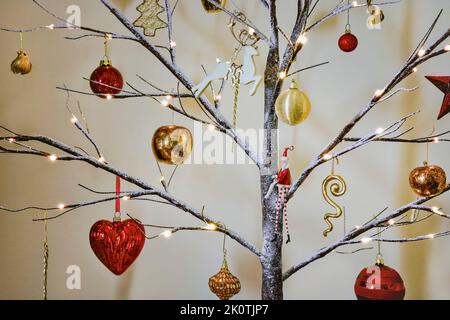 Weihnachtsbaumschmuck in traditionellem Rot und Gold hängt an einem modernen Zweig mit Schnee-Effekt Stockfoto