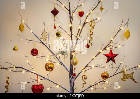 Weihnachtsbaumschmuck in traditionellem Rot und Gold hängt an einem modernen Zweig mit Schnee-Effekt Stockfoto